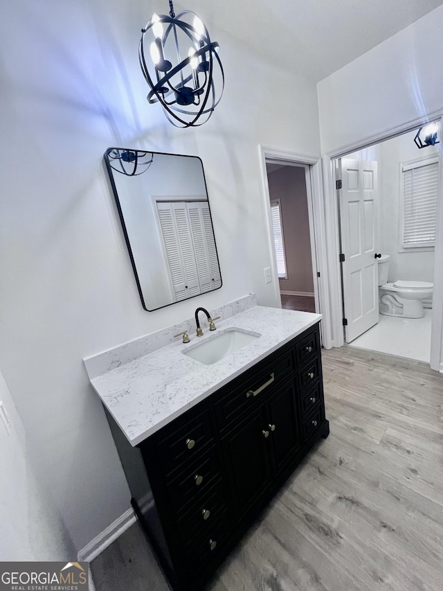 bathroom with toilet, wood finished floors, vanity, and a notable chandelier