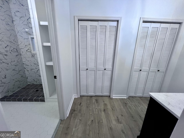 bathroom with baseboards, wood finished floors, a tile shower, vanity, and a closet