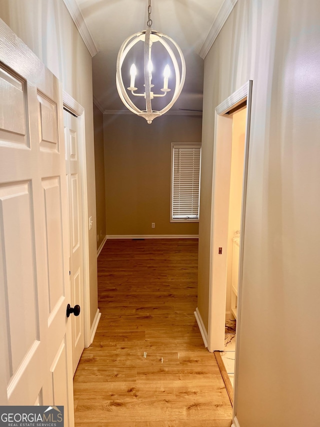 hallway with a chandelier, light wood-type flooring, crown molding, and baseboards