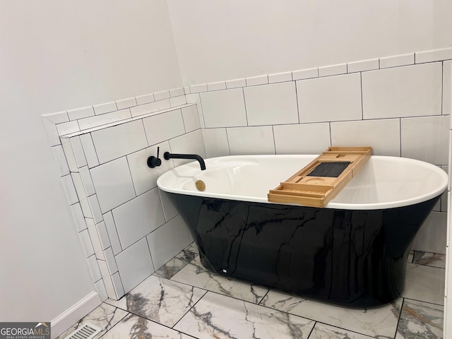 bathroom with a soaking tub, marble finish floor, and tile walls