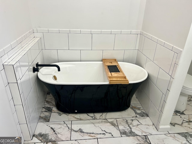 full bathroom with marble finish floor, a wainscoted wall, tile walls, a soaking tub, and toilet