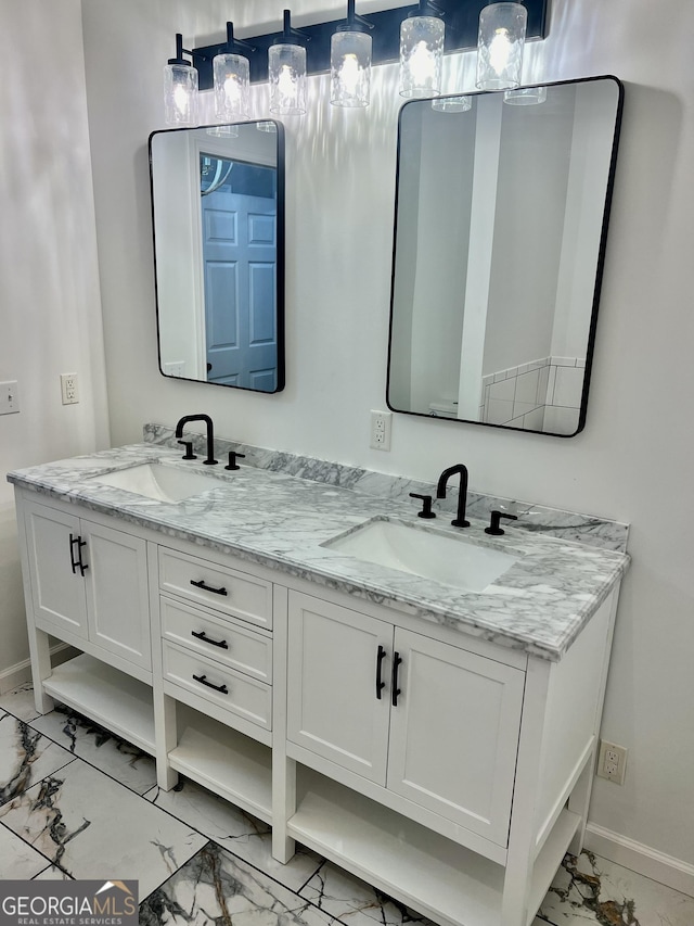 full bath featuring marble finish floor, double vanity, a sink, and baseboards