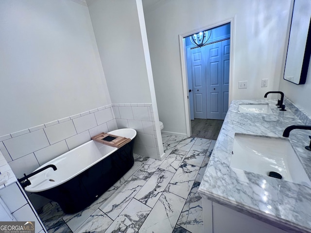 full bath featuring double vanity, marble finish floor, a freestanding bath, and a sink