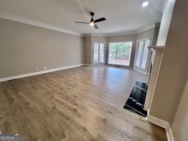 unfurnished living room with a fireplace, crown molding, light wood-style floors, a ceiling fan, and baseboards