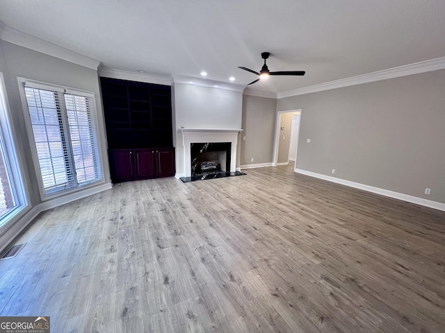 unfurnished living room with baseboards, visible vents, a fireplace with raised hearth, wood finished floors, and crown molding