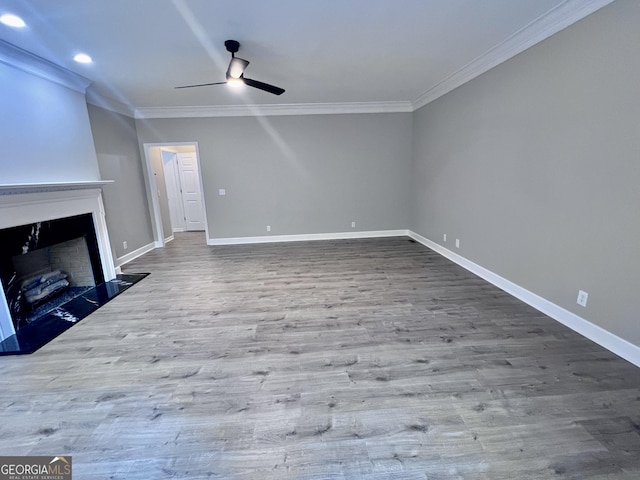 unfurnished living room featuring a fireplace with raised hearth, crown molding, baseboards, and wood finished floors