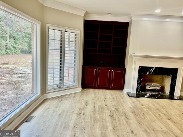 unfurnished living room with visible vents, baseboards, a premium fireplace, ornamental molding, and light wood-style floors