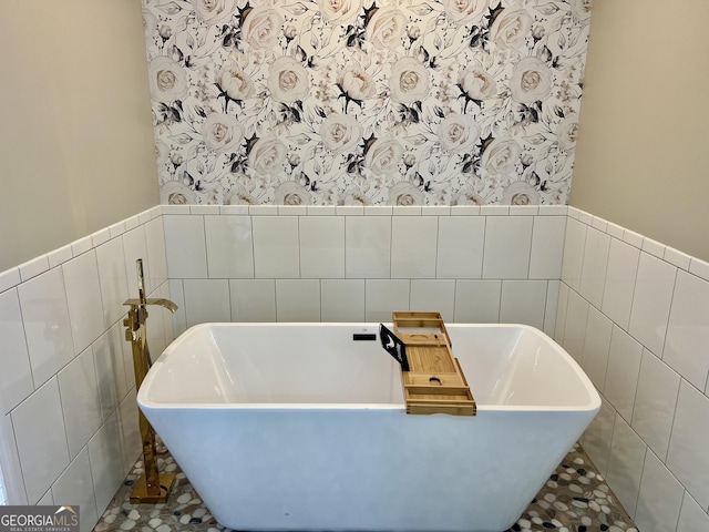 bathroom with a soaking tub, wallpapered walls, and wainscoting