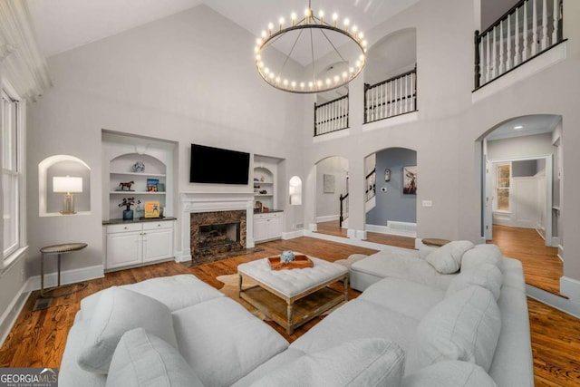 living room with high vaulted ceiling, hardwood / wood-style flooring, a high end fireplace, an inviting chandelier, and built in shelves