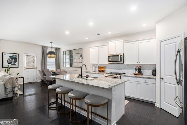 kitchen featuring white cabinetry, decorative light fixtures, a kitchen island with sink, and appliances with stainless steel finishes