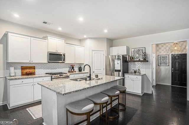 kitchen with sink, light stone counters, appliances with stainless steel finishes, a kitchen island with sink, and white cabinets