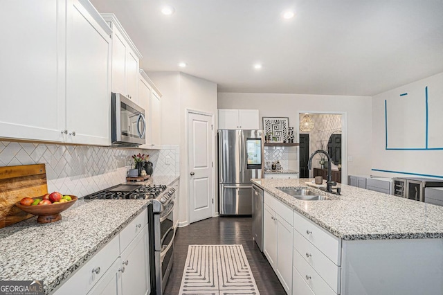 kitchen with sink, white cabinetry, light stone counters, appliances with stainless steel finishes, and an island with sink