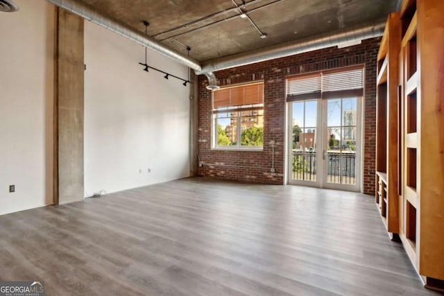 unfurnished room with a high ceiling, wood-type flooring, and brick wall