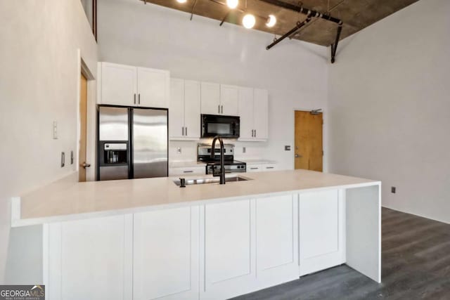 kitchen with dark wood-type flooring, appliances with stainless steel finishes, kitchen peninsula, a towering ceiling, and white cabinets