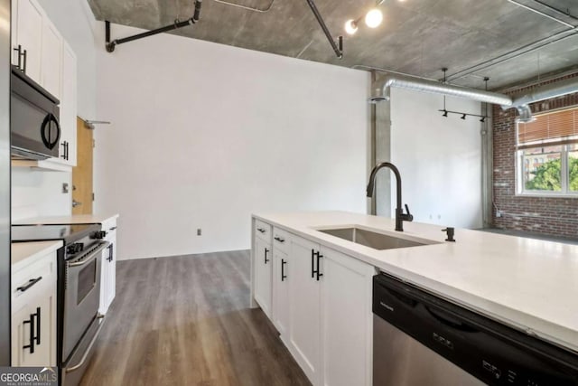 kitchen with sink, dark wood-type flooring, appliances with stainless steel finishes, white cabinets, and brick wall