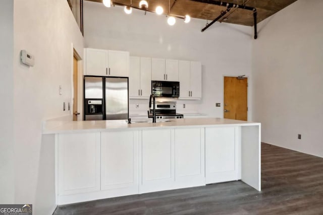 kitchen featuring a towering ceiling, stainless steel appliances, dark hardwood / wood-style flooring, and white cabinets