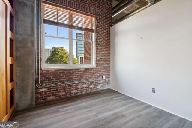 empty room with hardwood / wood-style floors and brick wall