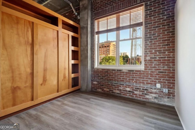 unfurnished room with brick wall and wood-type flooring