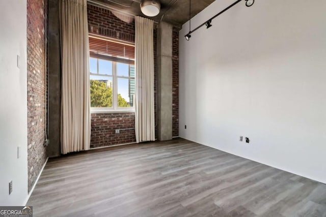 spare room featuring wood-type flooring, brick wall, and rail lighting