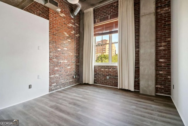 empty room with a towering ceiling, dark hardwood / wood-style floors, and brick wall