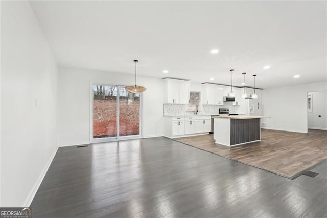 kitchen featuring appliances with stainless steel finishes, pendant lighting, tasteful backsplash, white cabinets, and a center island