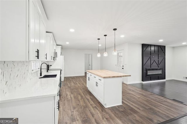 kitchen with butcher block counters, sink, white cabinetry, decorative light fixtures, and a kitchen island