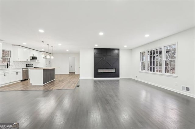 unfurnished living room featuring sink, a large fireplace, and dark hardwood / wood-style floors