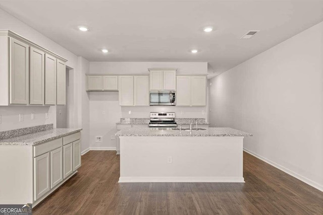 kitchen with appliances with stainless steel finishes, dark hardwood / wood-style floors, light stone countertops, and a center island with sink