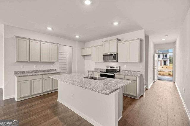 kitchen with a center island with sink, stainless steel appliances, light stone countertops, sink, and dark hardwood / wood-style floors