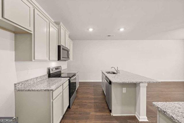 kitchen with a center island with sink, stainless steel appliances, dark hardwood / wood-style flooring, light stone countertops, and sink