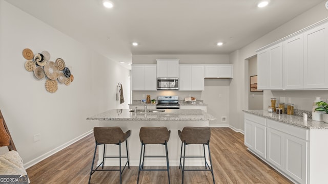 kitchen featuring an island with sink, appliances with stainless steel finishes, white cabinets, and light stone counters