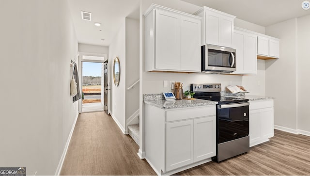 kitchen with white cabinets, light wood-type flooring, stainless steel appliances, and light stone counters