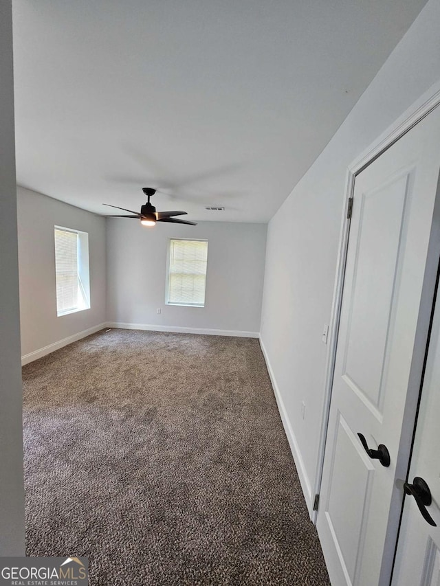 spare room featuring ceiling fan and dark colored carpet