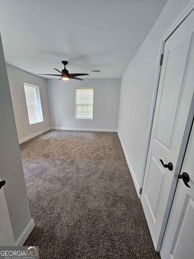 empty room with ceiling fan, a healthy amount of sunlight, and dark carpet