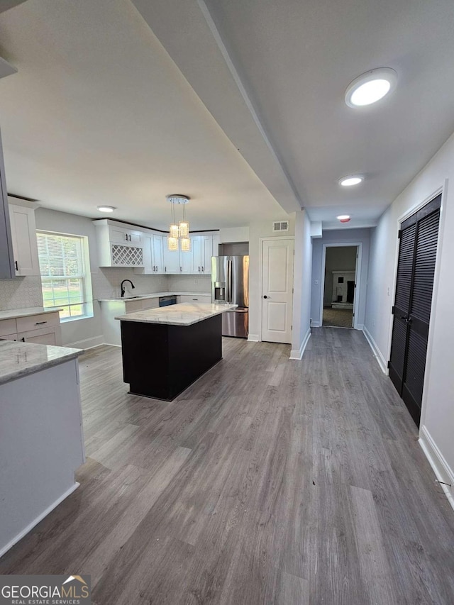 kitchen with pendant lighting, white cabinetry, stainless steel fridge, a center island, and light hardwood / wood-style floors