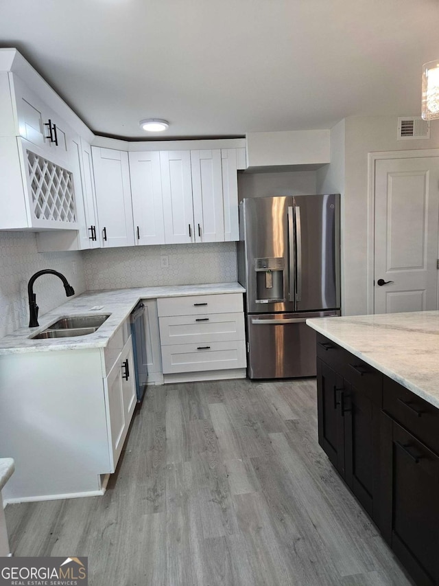 kitchen with appliances with stainless steel finishes, tasteful backsplash, sink, white cabinets, and light wood-type flooring