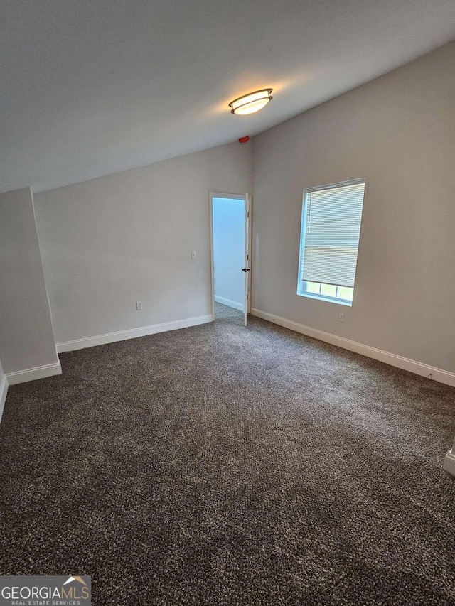 spare room with vaulted ceiling and dark colored carpet