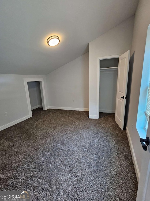 unfurnished bedroom with vaulted ceiling, a closet, and dark colored carpet