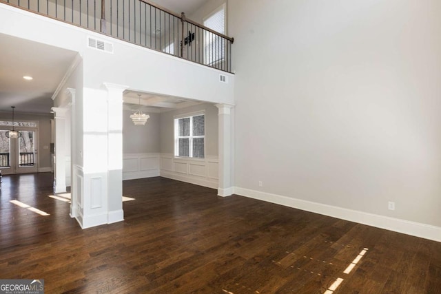 unfurnished living room with ornate columns, visible vents, a chandelier, and wood finished floors