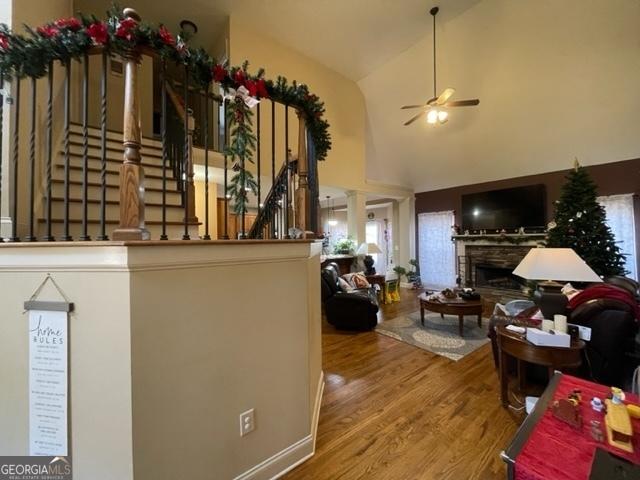 interior space featuring ornate columns, hardwood / wood-style floors, high vaulted ceiling, a fireplace, and ceiling fan