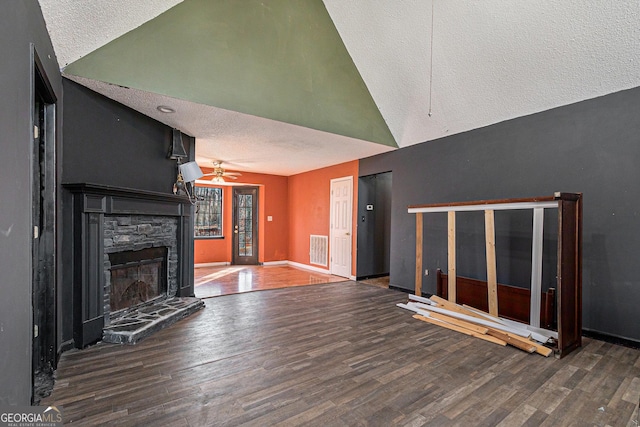 unfurnished living room featuring a stone fireplace, dark wood-type flooring, a textured ceiling, and ceiling fan