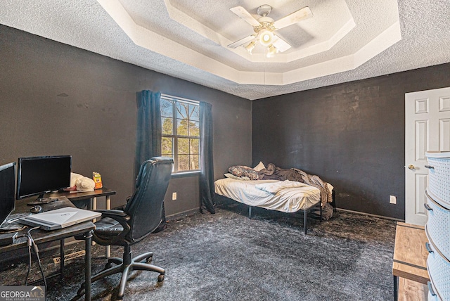 carpeted office with ceiling fan, a tray ceiling, and a textured ceiling