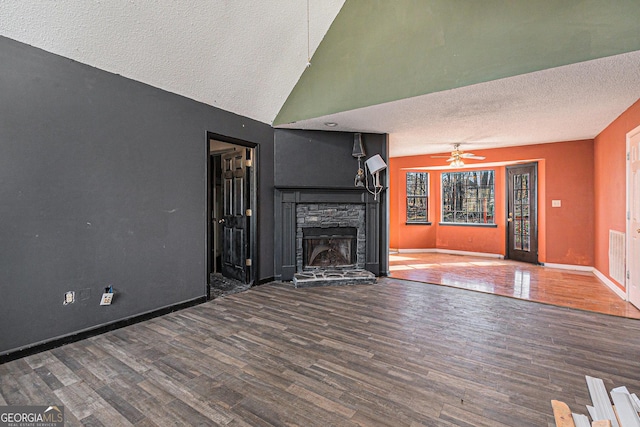 unfurnished living room featuring hardwood / wood-style floors, a stone fireplace, a textured ceiling, and ceiling fan