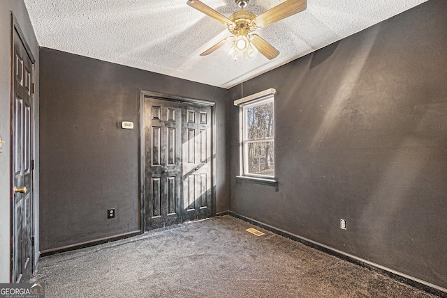 empty room featuring ceiling fan, a textured ceiling, and dark carpet