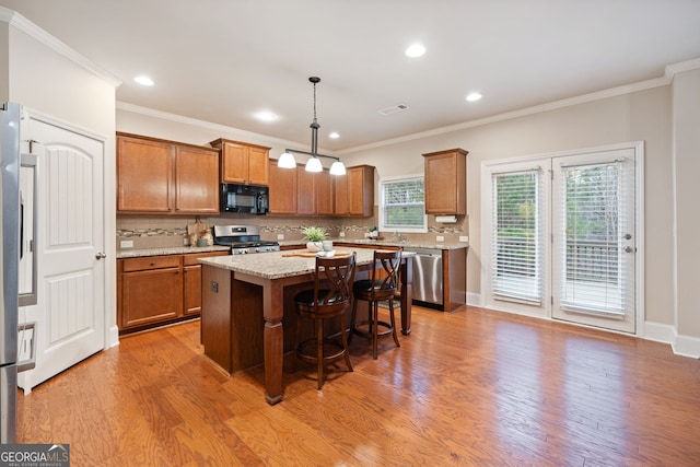 kitchen featuring a breakfast bar, appliances with stainless steel finishes, a kitchen island, pendant lighting, and light stone countertops