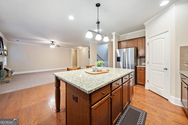 kitchen with pendant lighting, crown molding, light hardwood / wood-style flooring, a fireplace, and a kitchen island