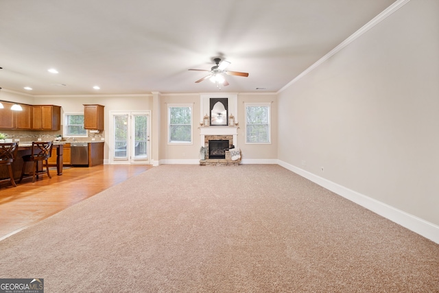 unfurnished living room featuring a stone fireplace, ornamental molding, light colored carpet, and ceiling fan