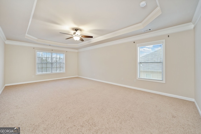 carpeted empty room with ceiling fan, plenty of natural light, a raised ceiling, and ornamental molding