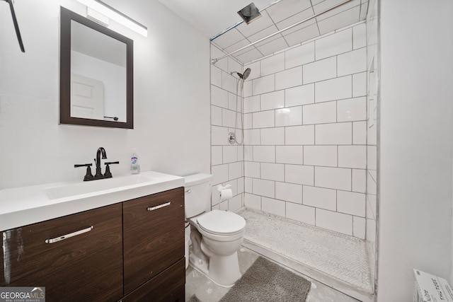 bathroom featuring vanity, a tile shower, and toilet