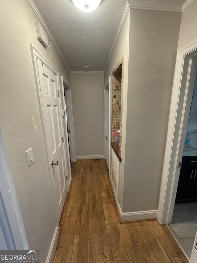 hall with wood-type flooring, ornamental molding, and a textured ceiling